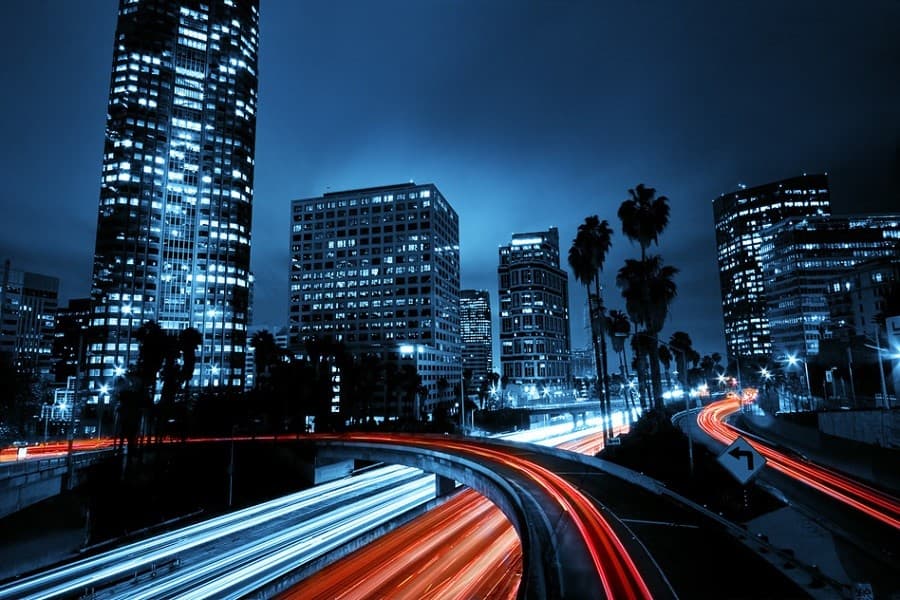 Innenstadt bei Nacht: Hochhäuser, Palmen und Lichtspuren des Verkehrs auf einer Stadtautobahn